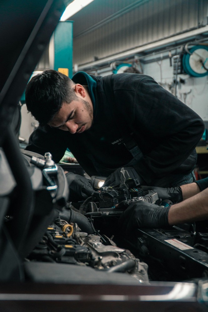 Mechanic leaning over an engine bay, working by drop light